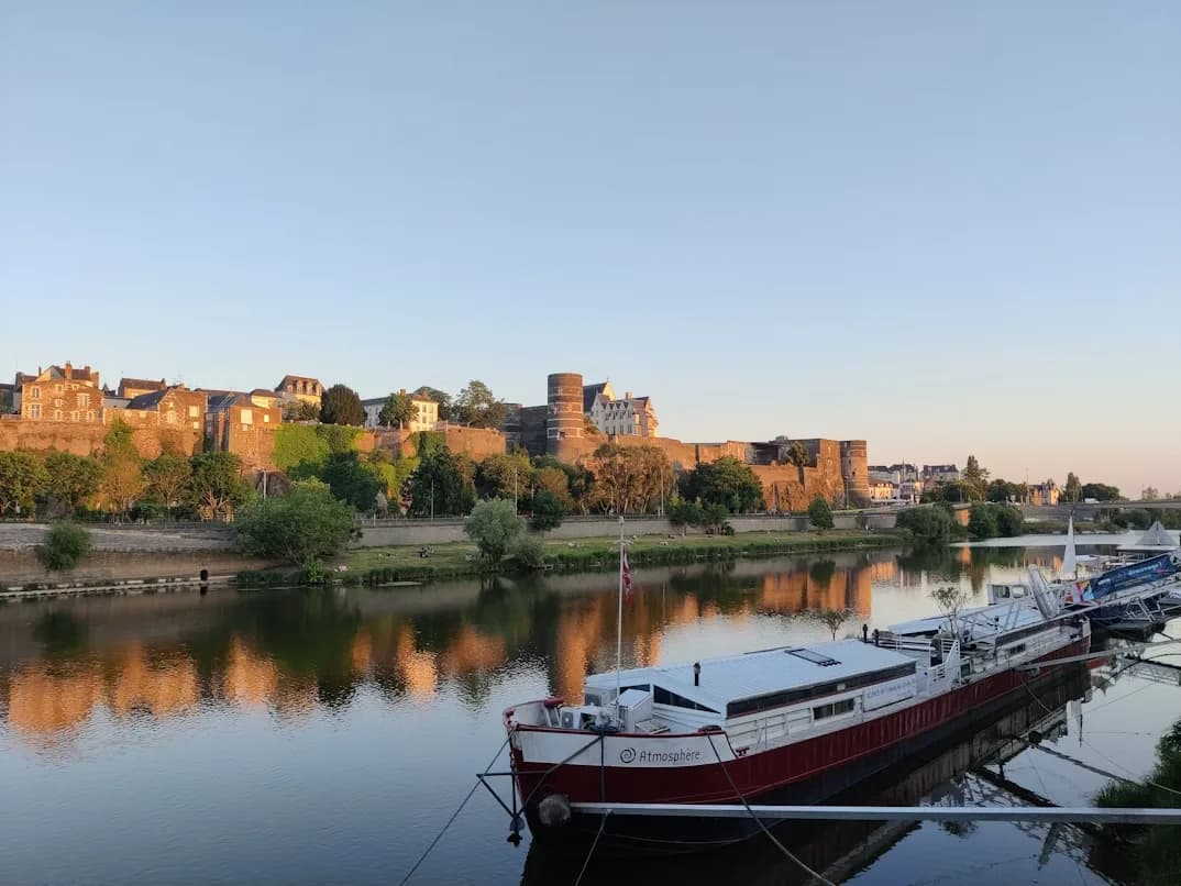 A wide river with a moored boat and historic buildings on its banks is a beautiful sight at sunset.