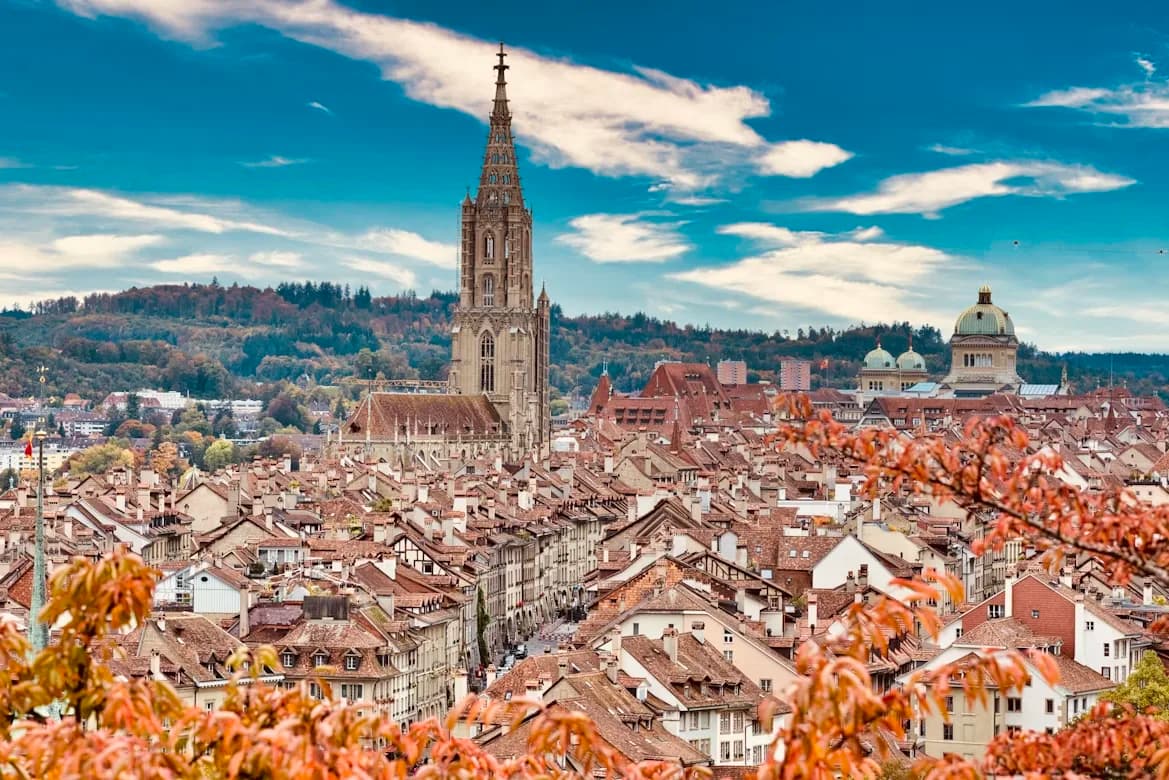 The historic Zytglogge clock tower rises above the old town of Bern, with its red rooftops and a distant view of the Federal Palace.