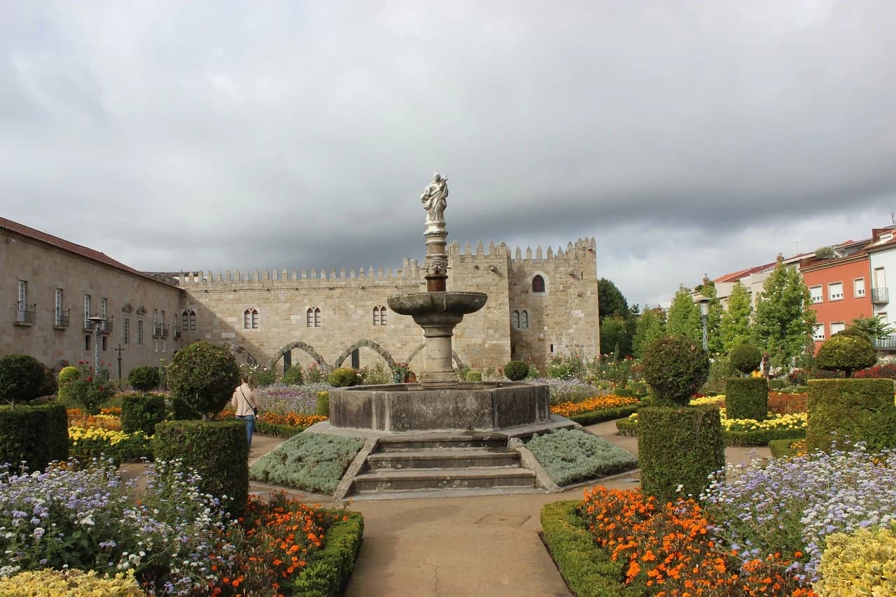 A formal garden with a large fountain and manicured bushes is a beautiful sight in front of the historic Braga Cathedral.