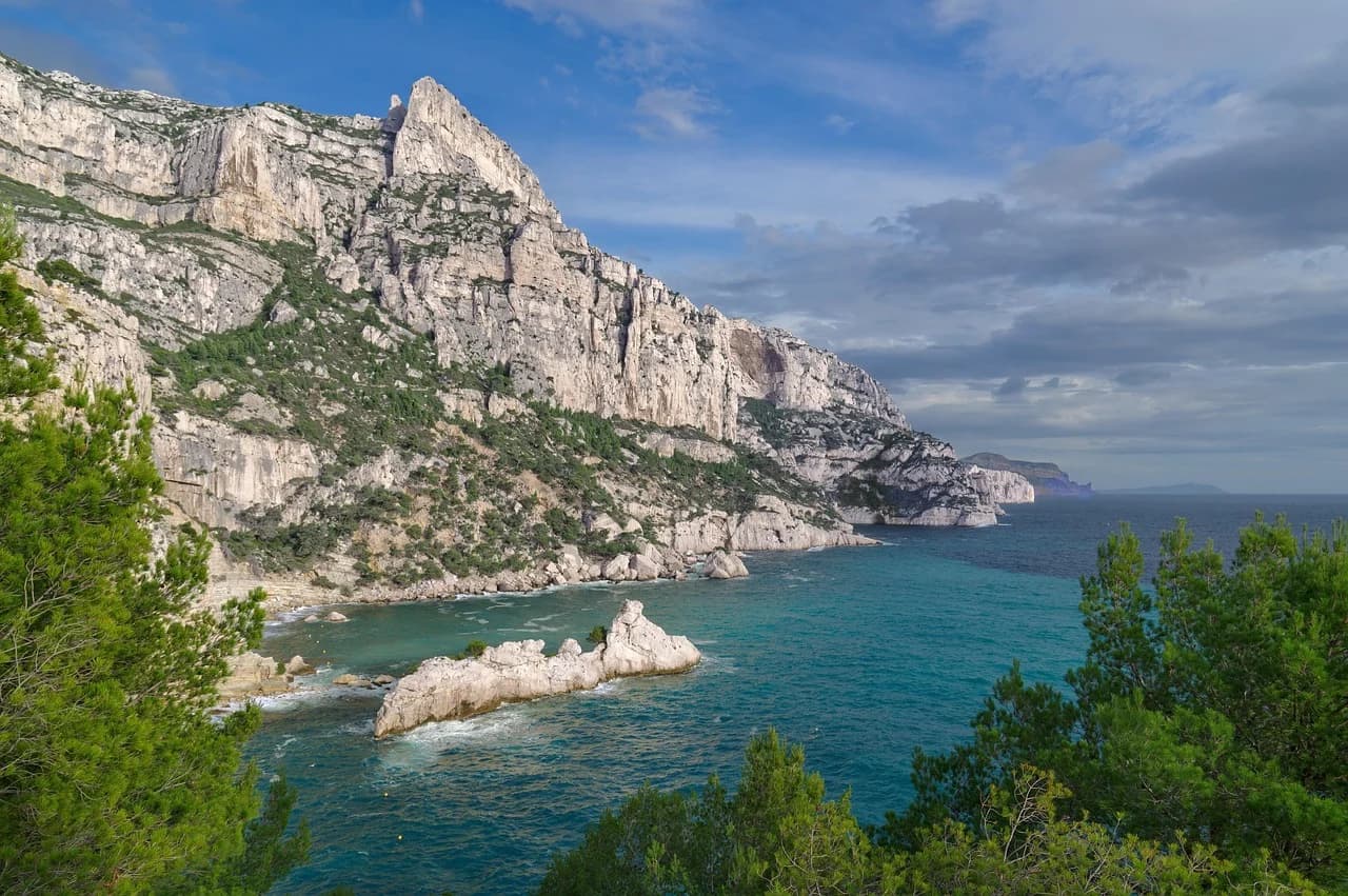 The towering white cliffs of a Calanque drop into the turquoise waters of the Mediterranean, creating a dramatic coastal landscape.
