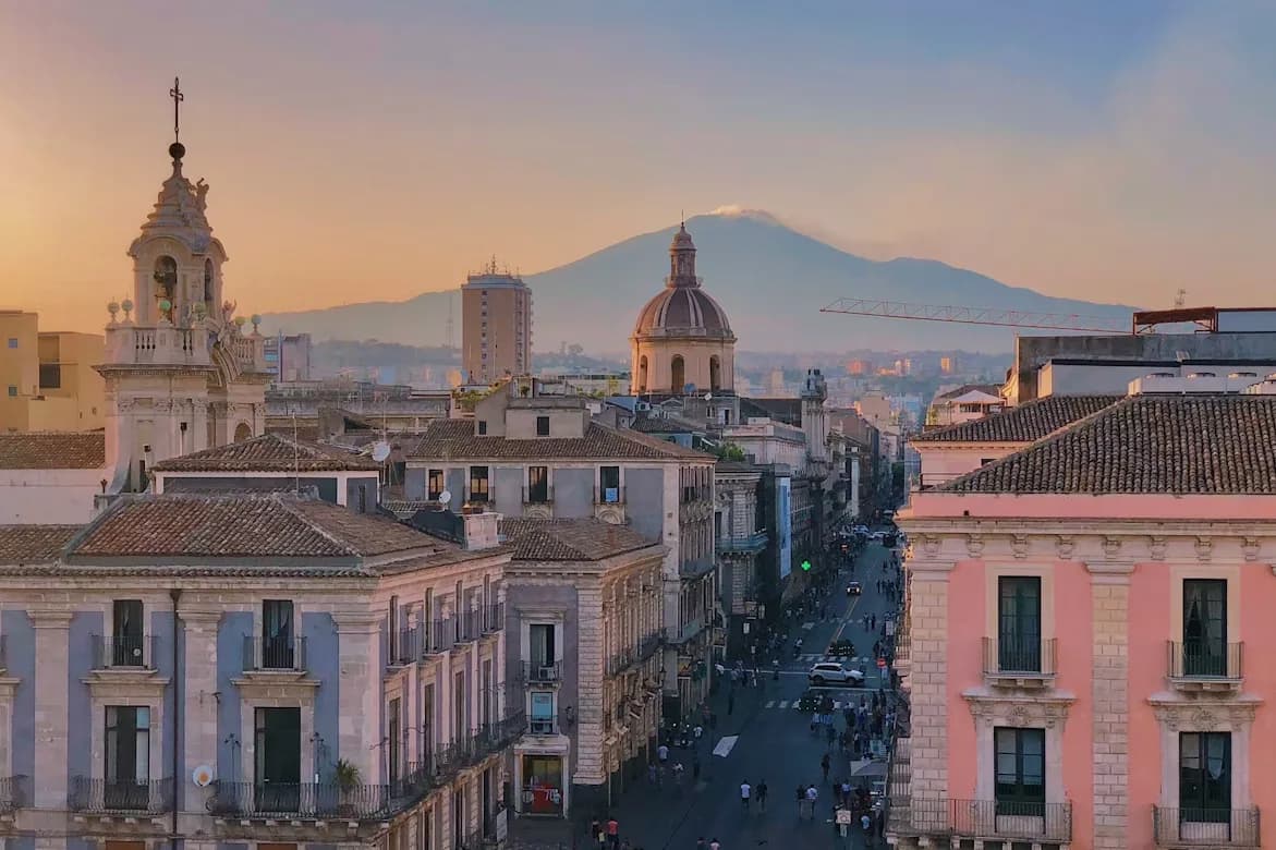 The famous Mount Etna stands majestically in the distance, providing a dramatic backdrop to the historic city of Catania.
