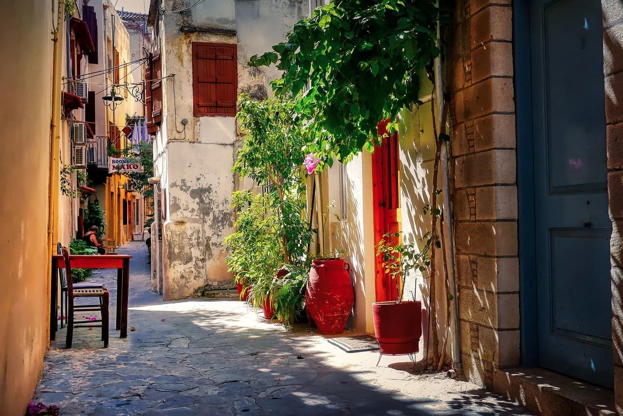 A narrow, charming alleyway in the Old Town of Chania is lined with traditional buildings and lush potted plants.