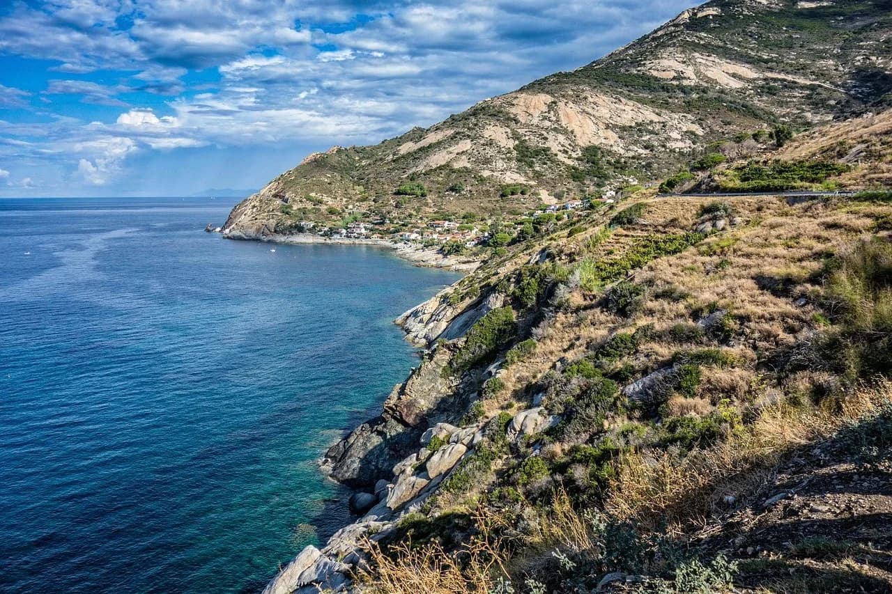 The stunning coastline of Elba is captured from a high vantage point, with the rugged mountains meeting the crystal-clear blue sea.