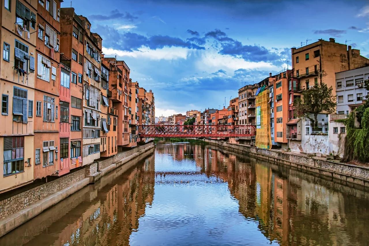 The colorful houses along the Onyar River are beautifully reflected in the water, with the iconic red bridge connecting the two sides of the city.