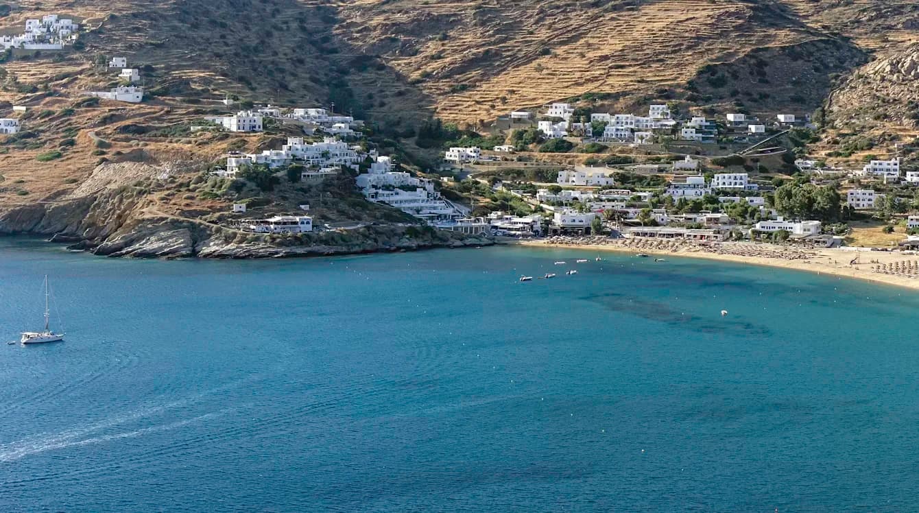 A peaceful bay on the island of Ios is bordered by a long sandy beach and a hillside dotted with traditional white buildings.