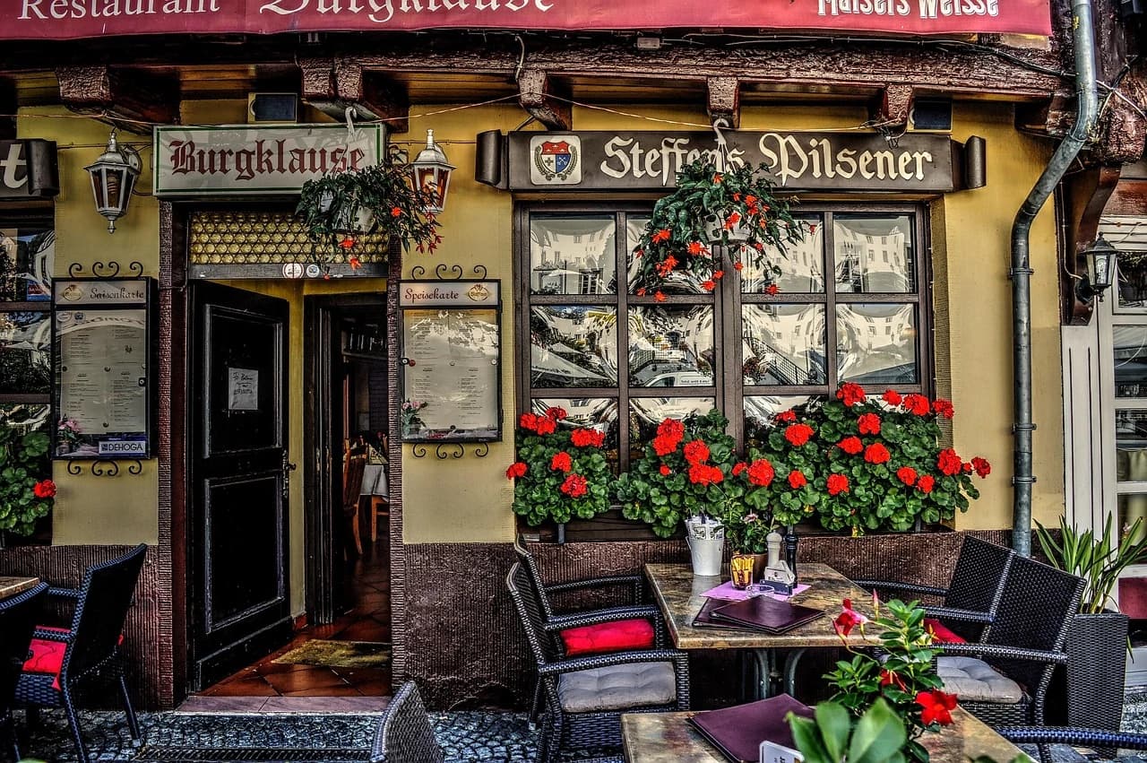 The rustic facade of a traditional German pub with a beer sign and hanging flower pots creates an inviting scene.