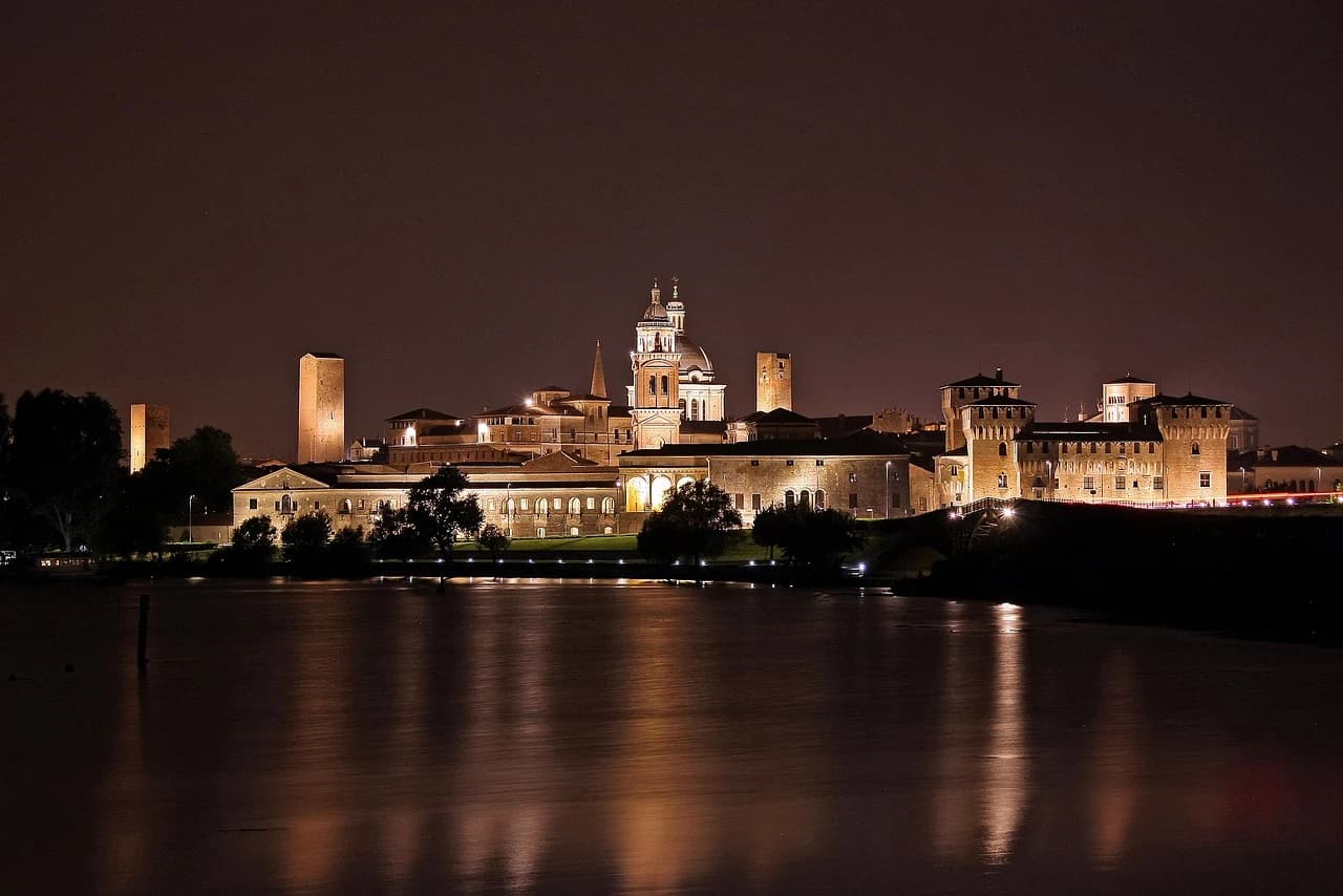 The illuminated skyline of Mantua, with its historic domes and towers, is a beautiful sight at night, reflected on the still waters of the lake.