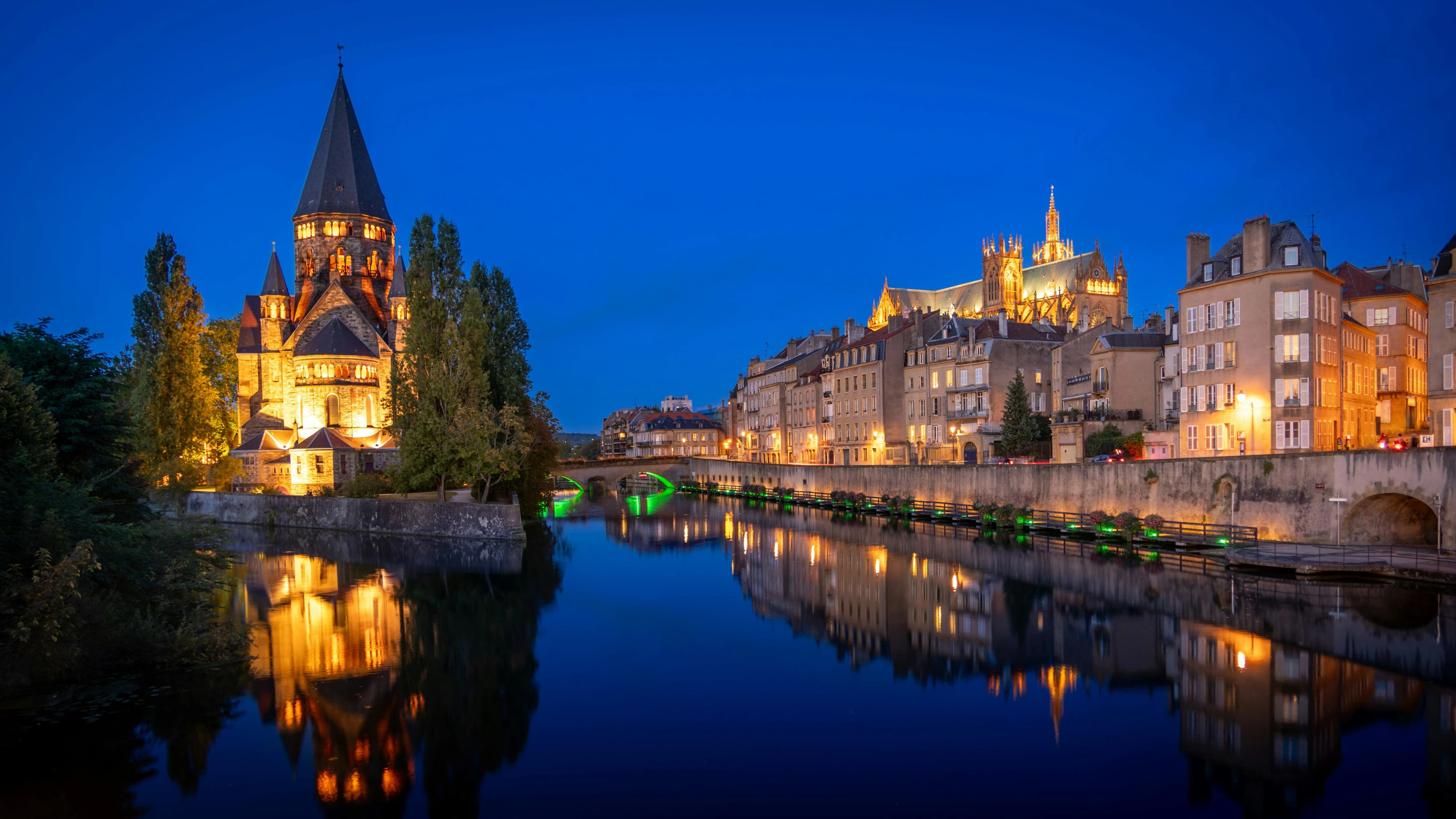 The Temple Neuf, a beautiful Protestant church, and the Saint-Étienne Cathedral are illuminated at night, their reflections shimmering on the water.