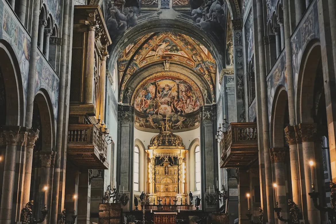 The grand, majestic interior of the Parma Cathedral features a high, vaulted ceiling with intricate frescoes and a golden altar.