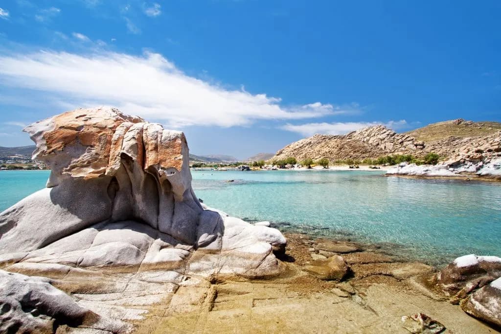 Large, smooth rock formations create a natural barrier on a sandy beach with crystal-clear turquoise water.