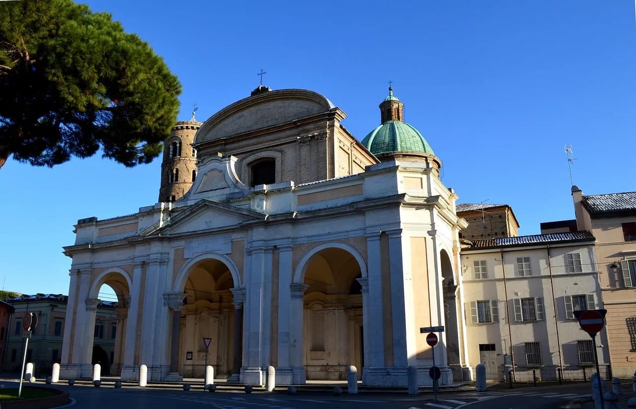 The elegant facade of the Basilica di San Vitale, a masterpiece of Byzantine architecture, stands against a clear blue sky.