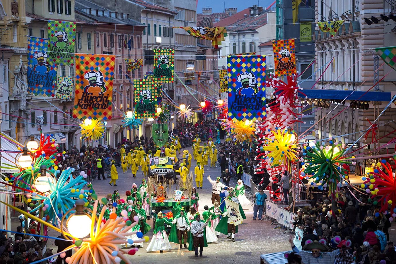 A colorful carnival procession with people in elaborate costumes and floats fills a city street.
