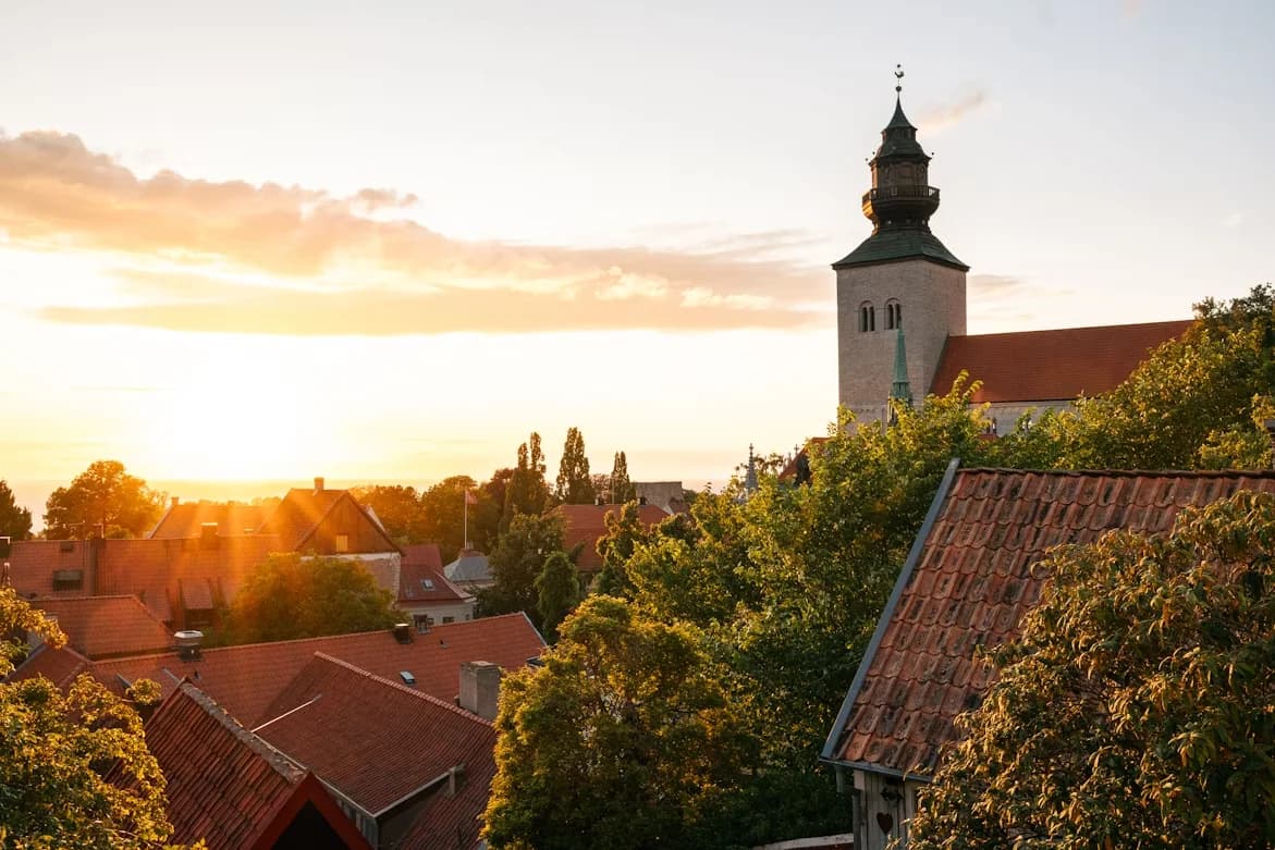 The skyline of Visby is bathed in the warm light of a sunset, highlighting the historic buildings and the stunning steeple of a local church.