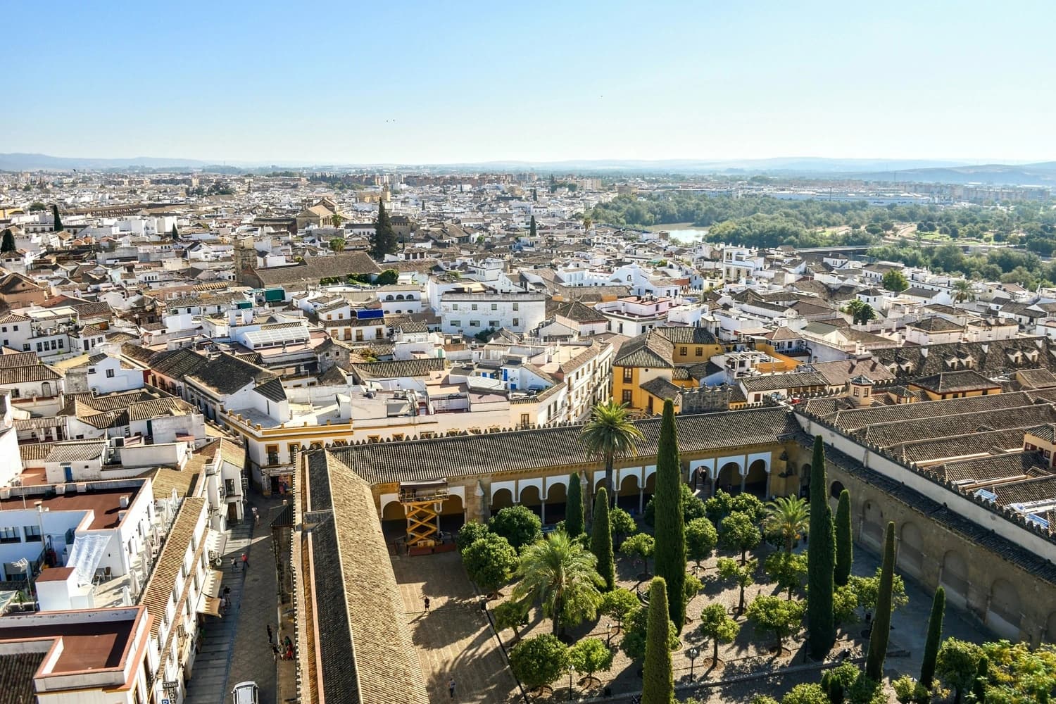 The historic heart of Córdoba, Spain, stretching out under the Andalusian sun. From this viewpoint, you can appreciate the dense, ancient layout and the green oasis of the Mezquita's Orange Tree Courtyard
