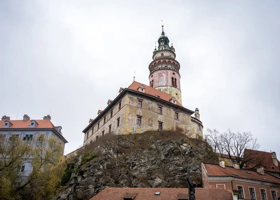 The historic Český Krumlov Castle and its tower stand on a rocky hill, overlooking the town below.