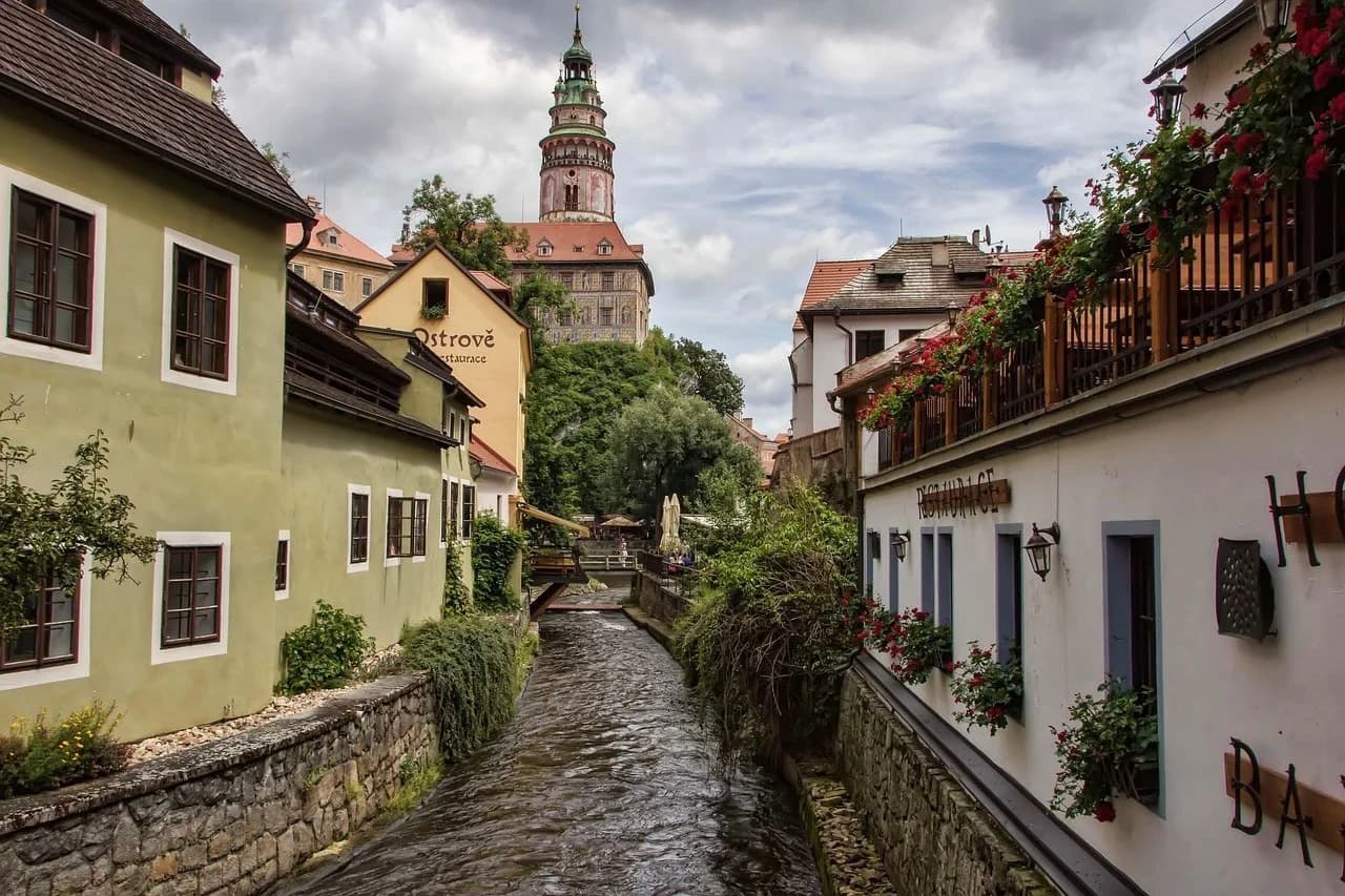 A serene stream flows through a narrow valley, with historic buildings and charming restaurants on either side.