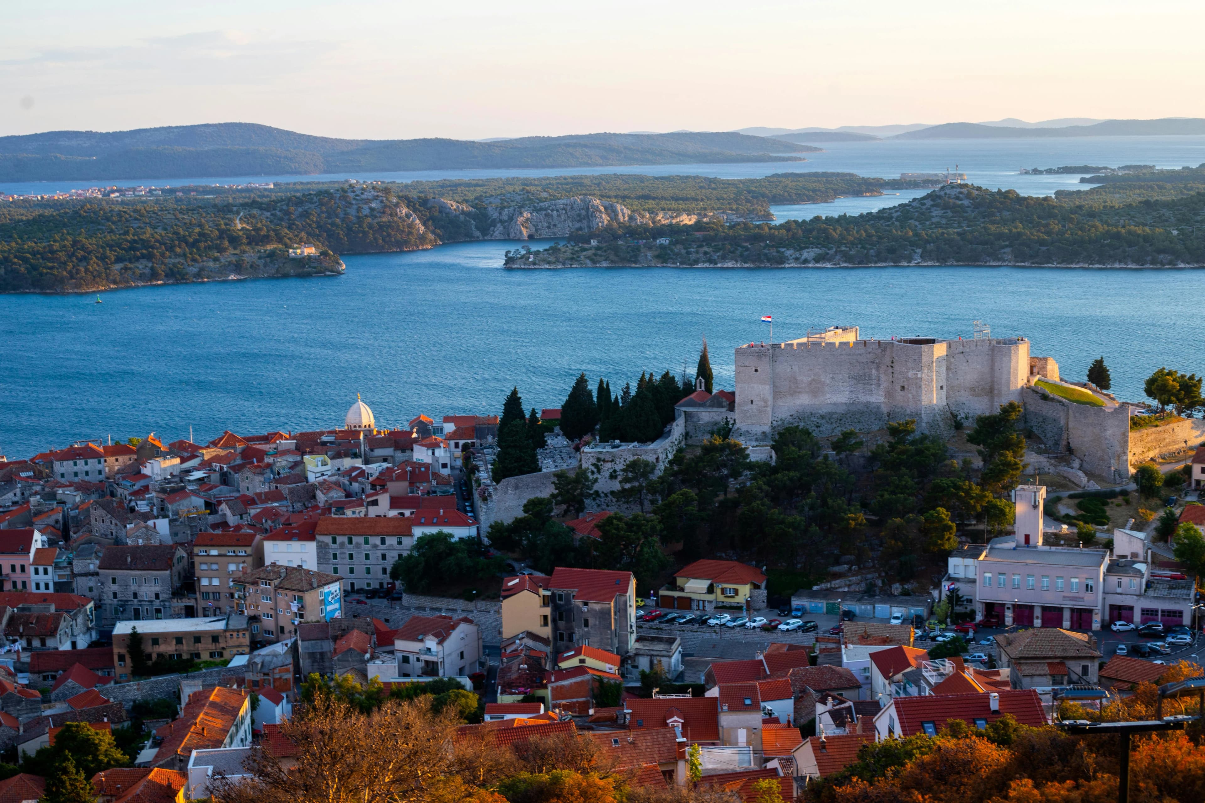 An aerial view captures the historic fortress of St. Michael's and the city of Šibenik, with the Adriatic Sea and numerous islands in the distance.