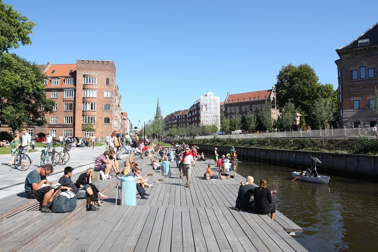 Locals and visitors alike relax on the wooden decks along the Aarhus River, a popular spot in the city center for enjoying the sun and the scenery.