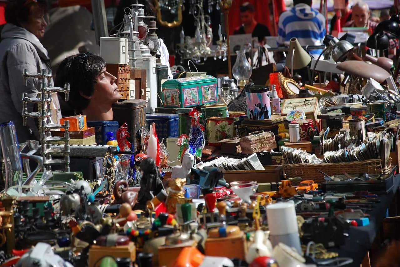 A large, bustling flea market is filled with stalls overflowing with antiques, trinkets, and various second-hand items.