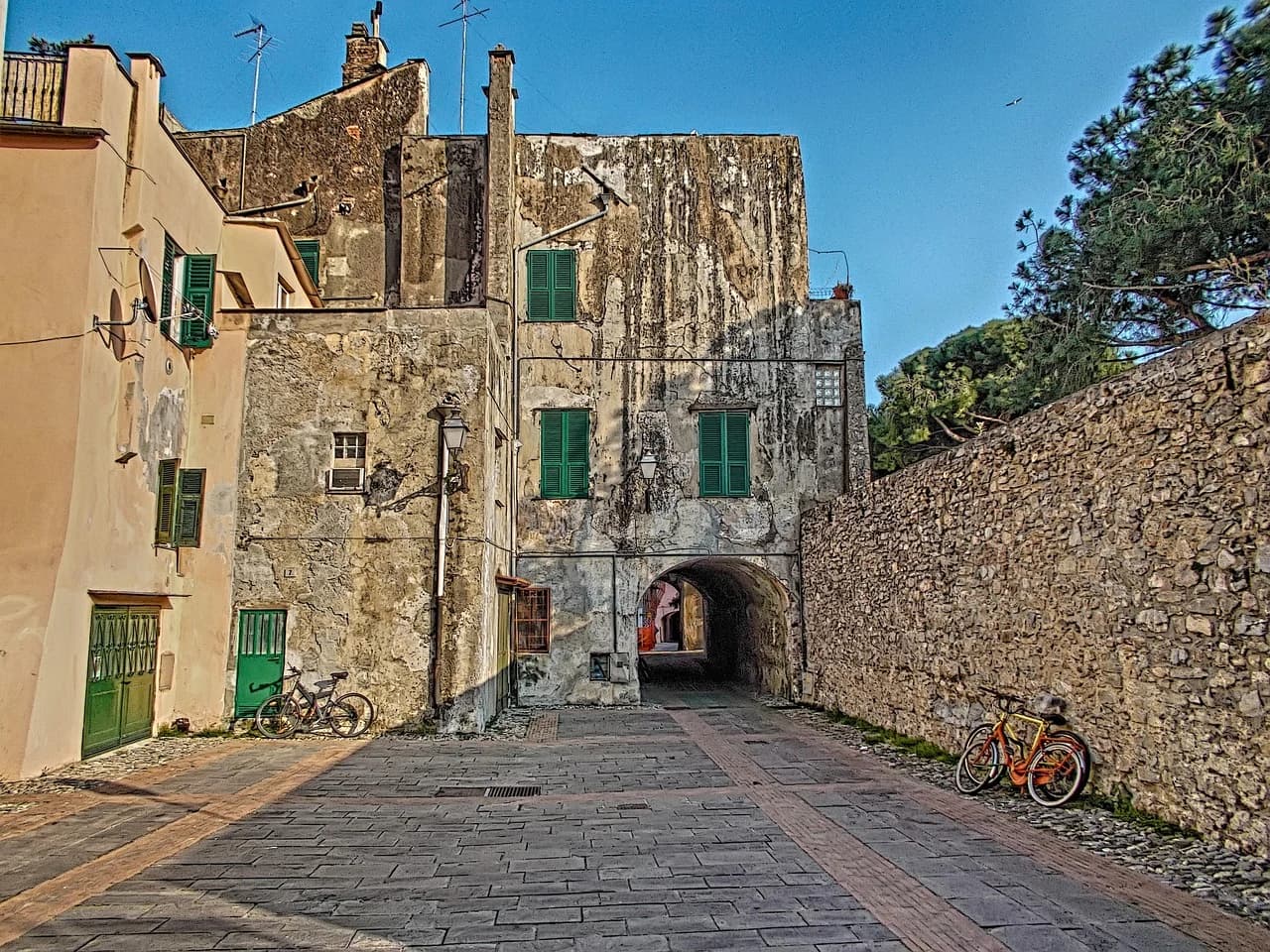 A narrow, cobblestone alleyway with a historic archway is lined with old stone buildings and a few bicycles.