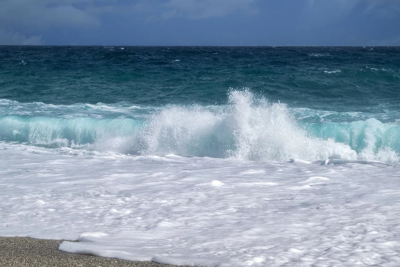 Large, white waves crash onto a sandy beach, with the deep blue sea stretching to the horizon.