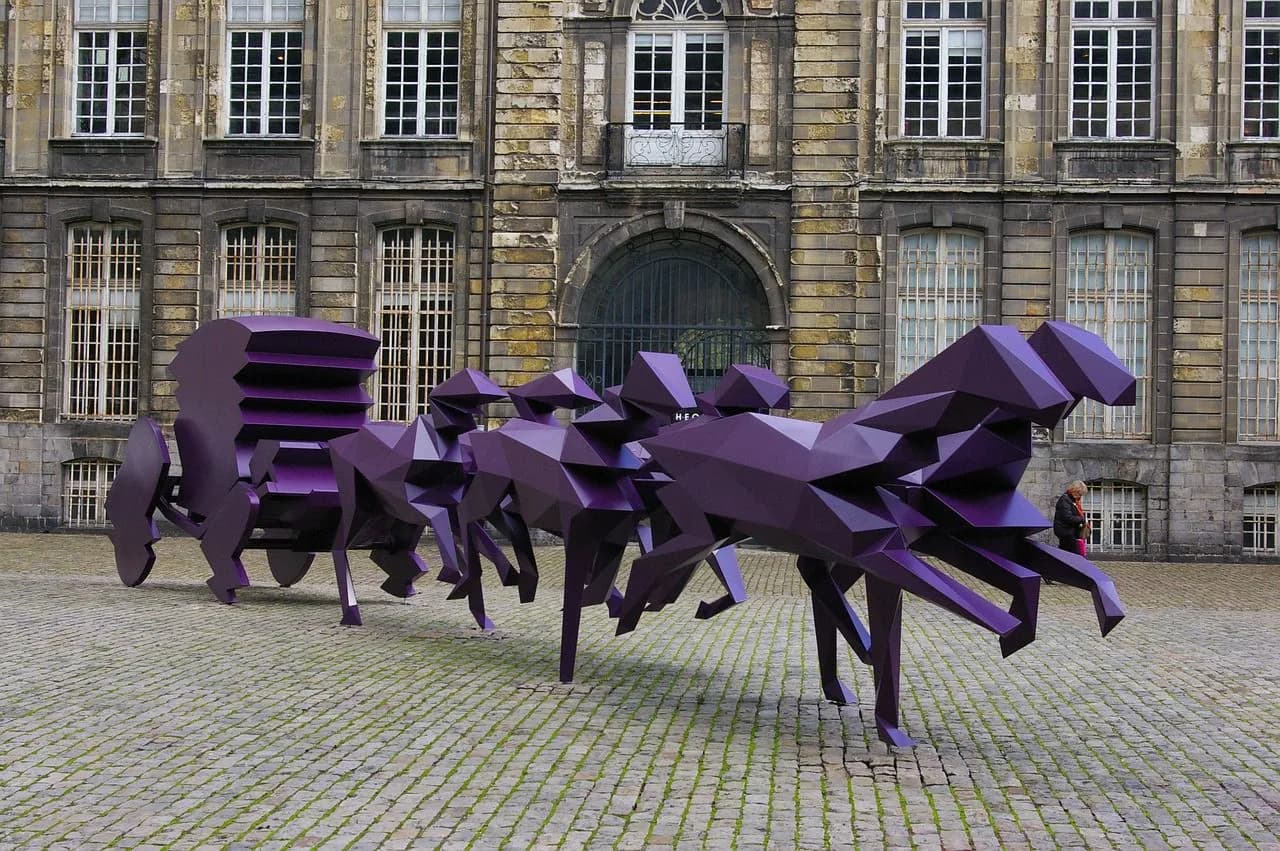 A unique, modern sculpture of a purple horse-drawn carriage sits in a cobblestone square in front of a historic building.