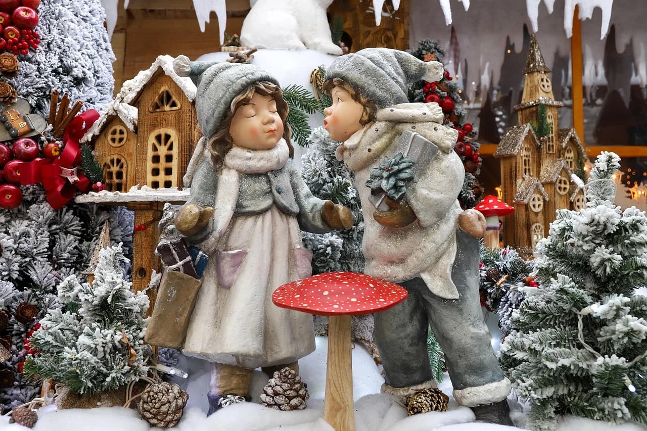 A festive Christmas display with figurines of children and decorated trees is set up in a snowy landscape.