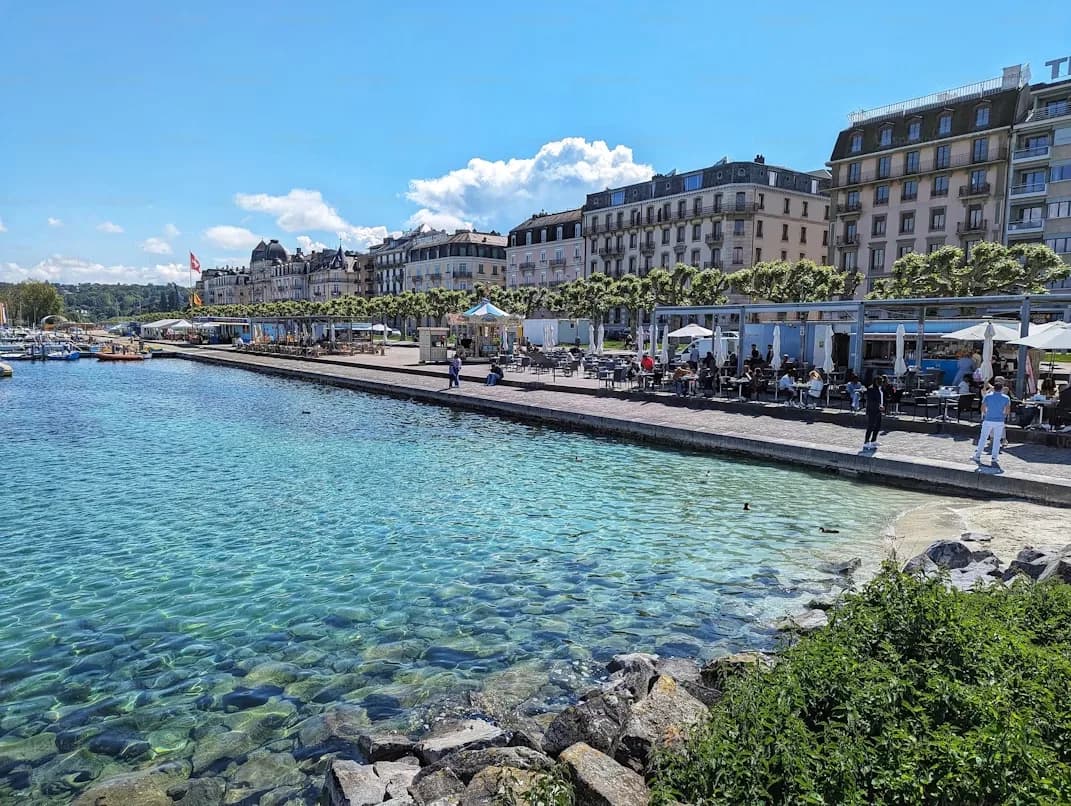 A serene canal is lined with restaurants and historic buildings, with people relaxing at outdoor tables on a sunny day.