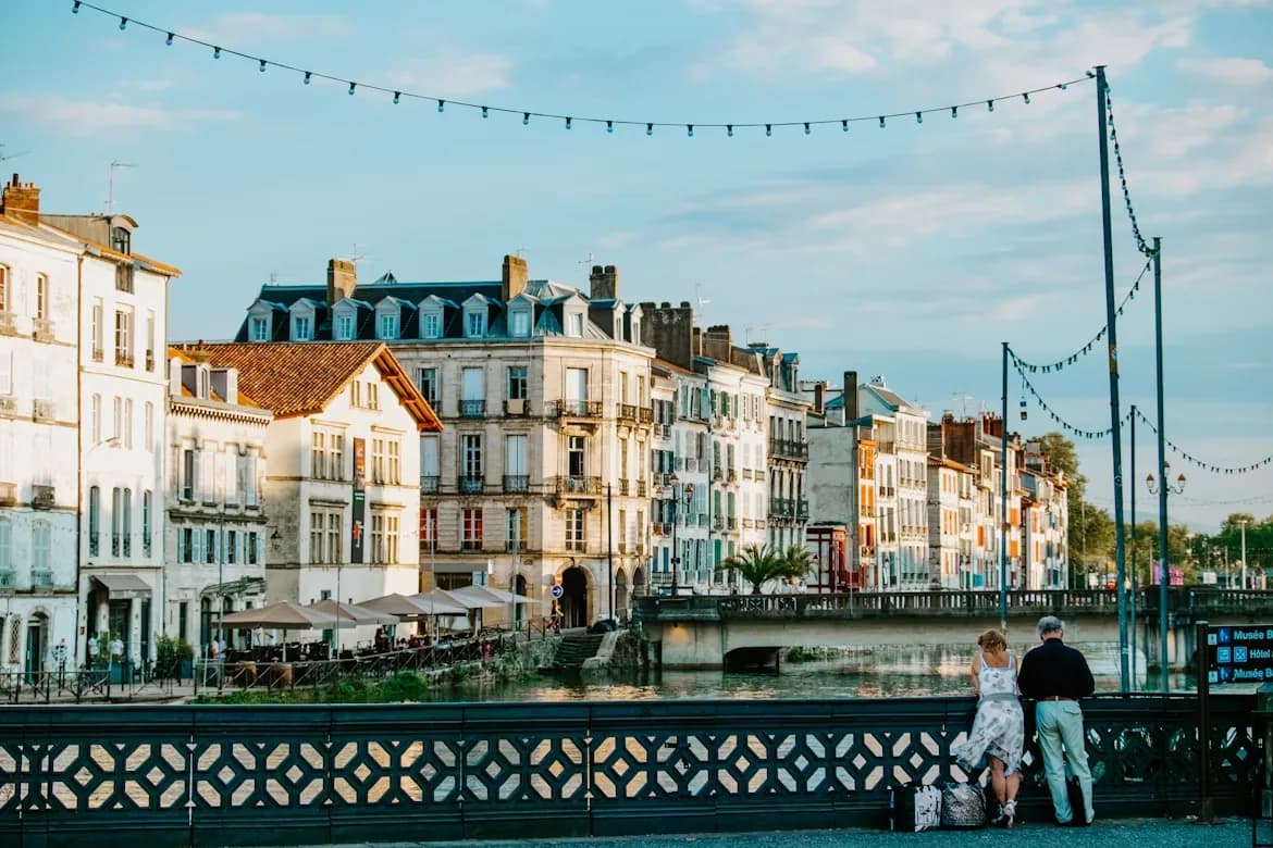 A charming waterfront in Bayonne is bustling with people and is lined with traditional Basque houses and string lights.