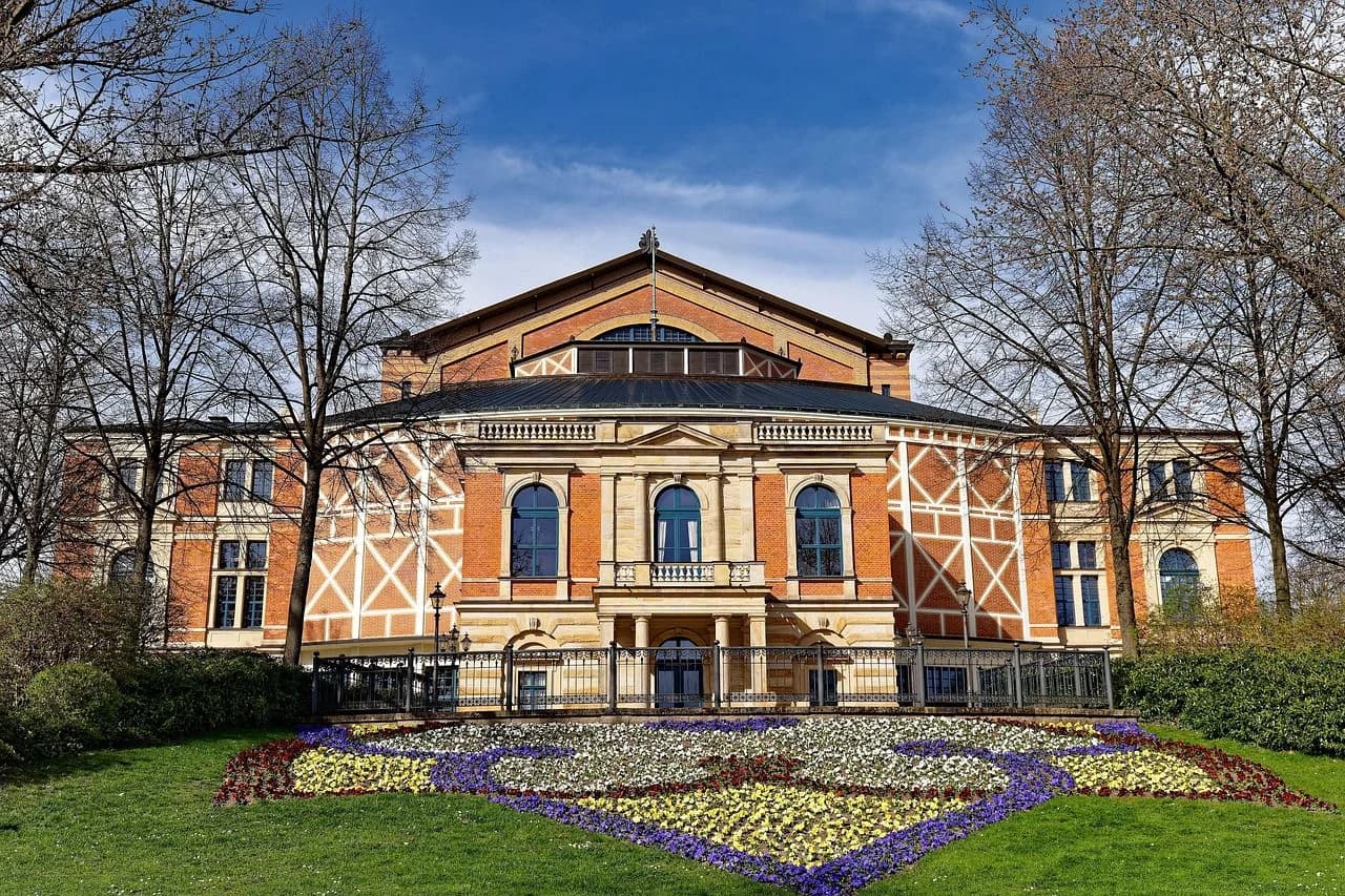 The magnificent red brick facade of the Bayreuth Festspielhaus, a world-famous opera house, is surrounded by a beautiful garden.