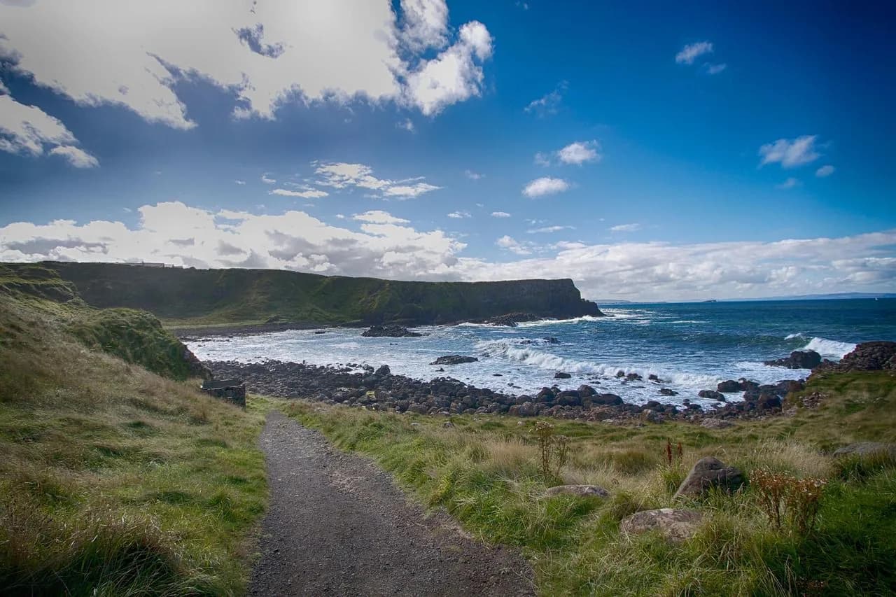 A scenic coastal path winds along a rugged cliffside, with the crashing waves of the Atlantic Ocean in the background.