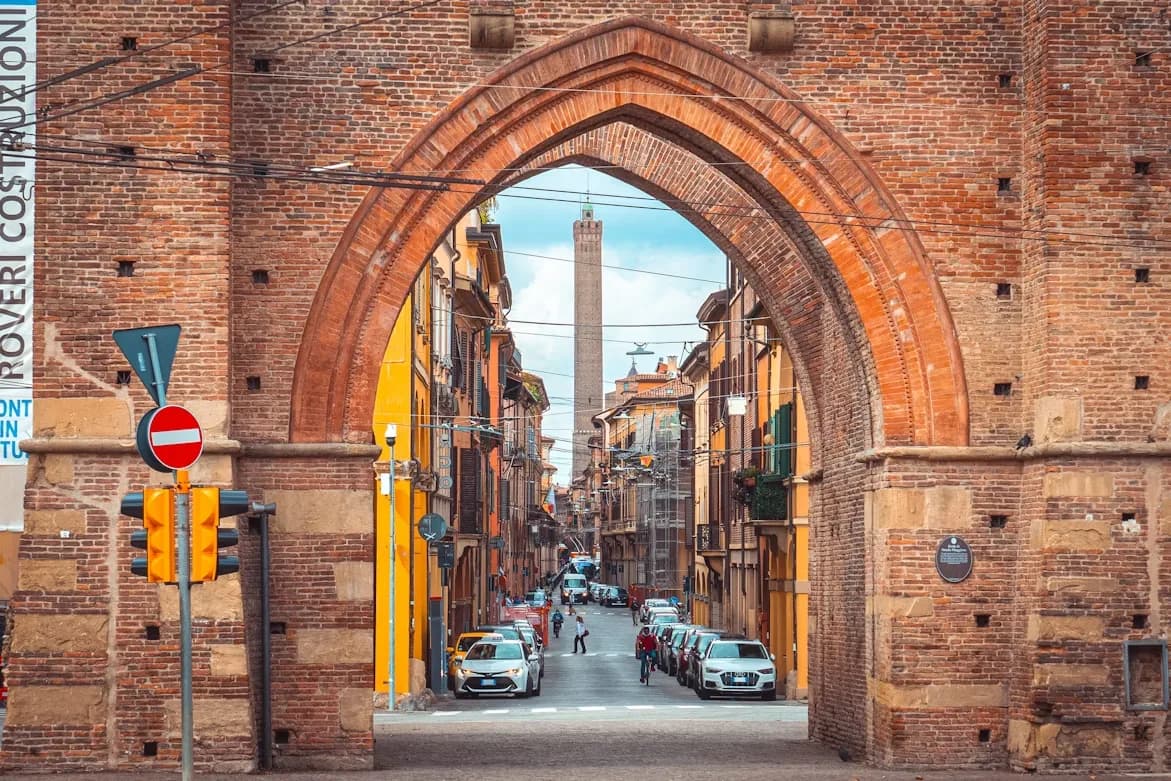A medieval brick archway frames a view of a bustling street leading toward the famous Due Torri, or Two Towers.