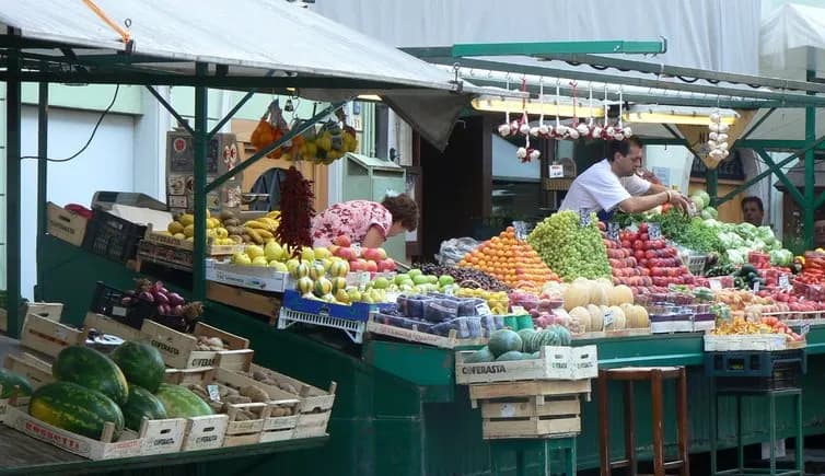 A food market in a bustling square is overflowing with a wide variety of fresh fruits and vegetables.