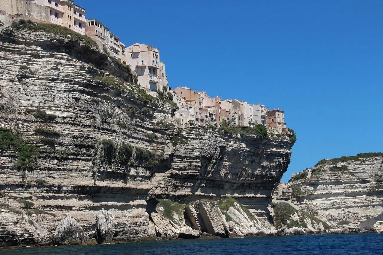 The historic buildings of Bonifacio are perched precariously on the edge of a towering white cliff, with the sea below.