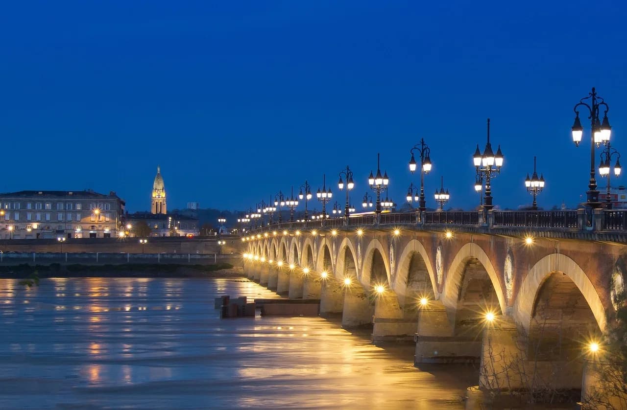 The Pont de Pierre, a historic stone bridge with illuminated arches, spans the Garonne River at night.