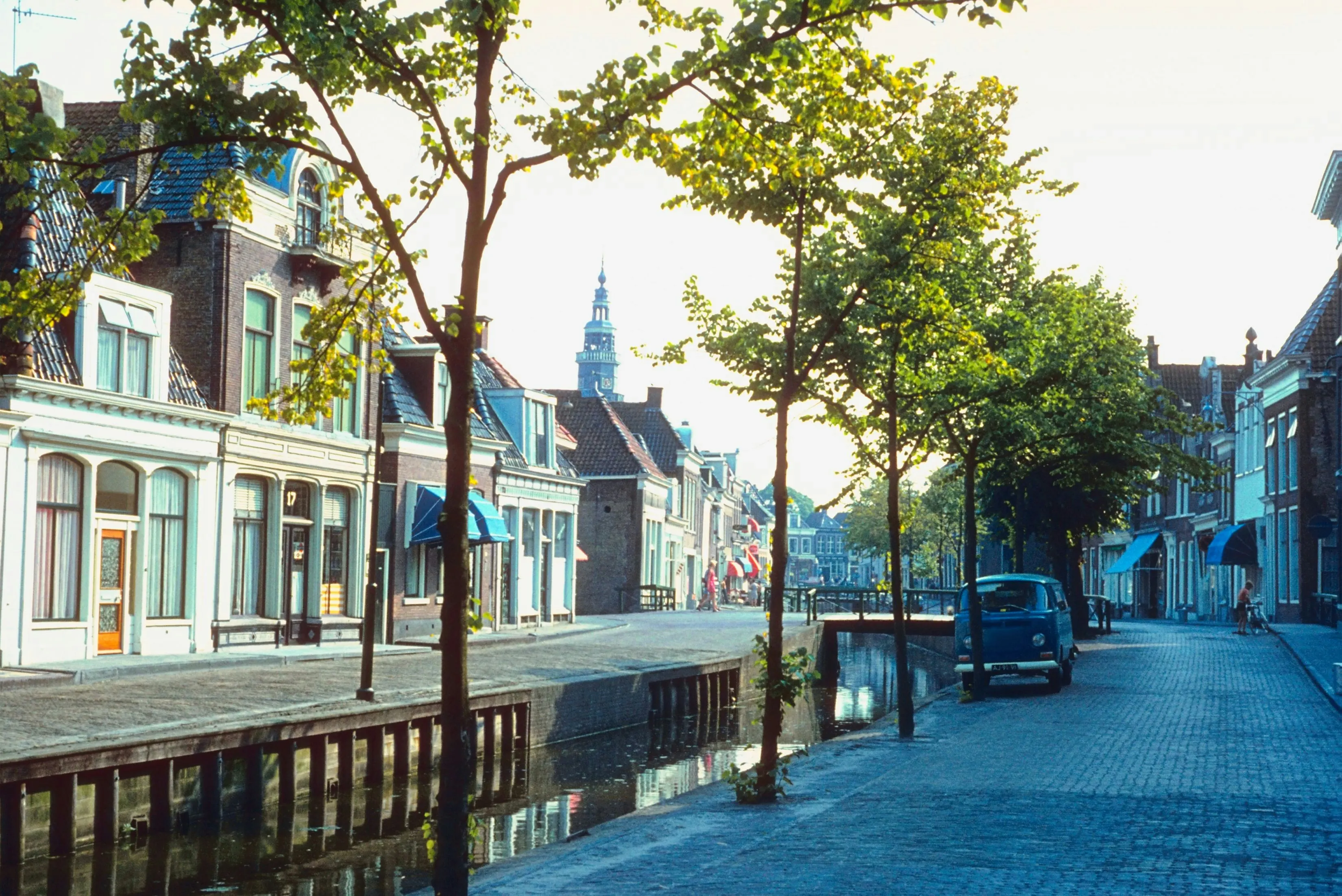 A quiet cobblestone street in Breda is lined with traditional Dutch buildings and trees, with a distant church steeple.