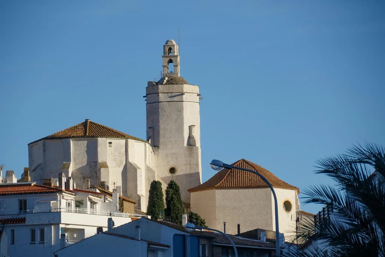 A traditional white church with a bell tower rises above the rooftops of the town, set against a clear blue sky.