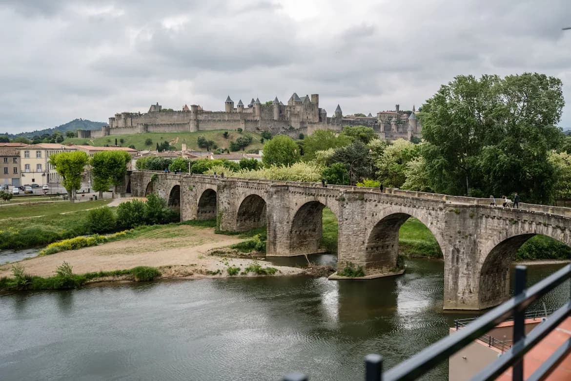 The Pont Vieux, a medieval bridge with stone arches, crosses the Aude River and leads to the fortified city of Carcassonne.