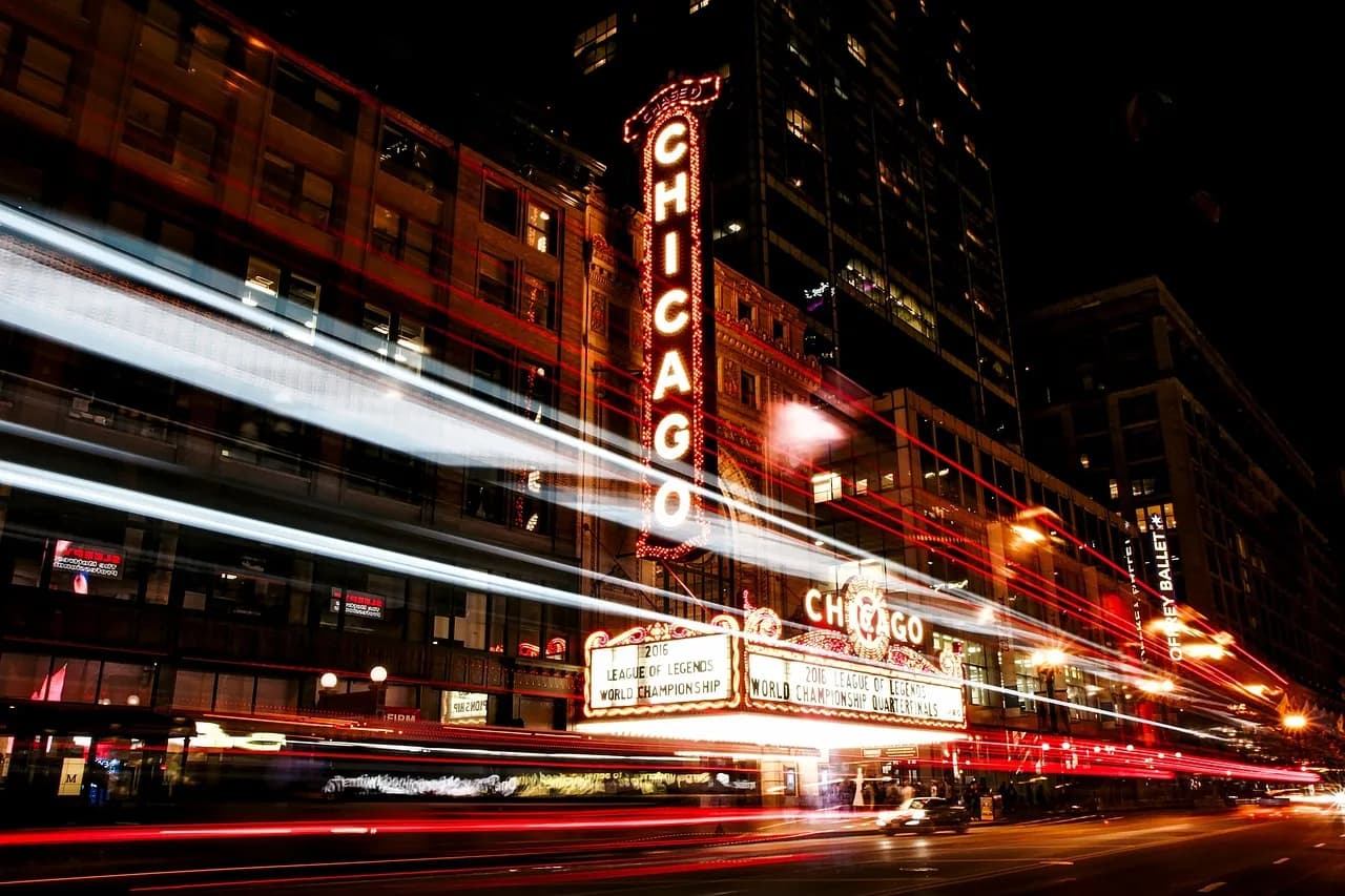 The vibrant Chicago Theatre sign glows brightly against the night sky, with streaks of light from passing cars creating a dynamic urban scene.