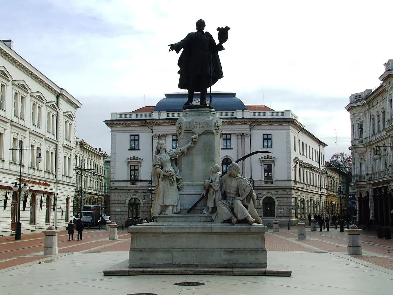 A grand statue of a historical figure on a pedestal is a focal point in a large, open square, surrounded by elegant historic buildings.