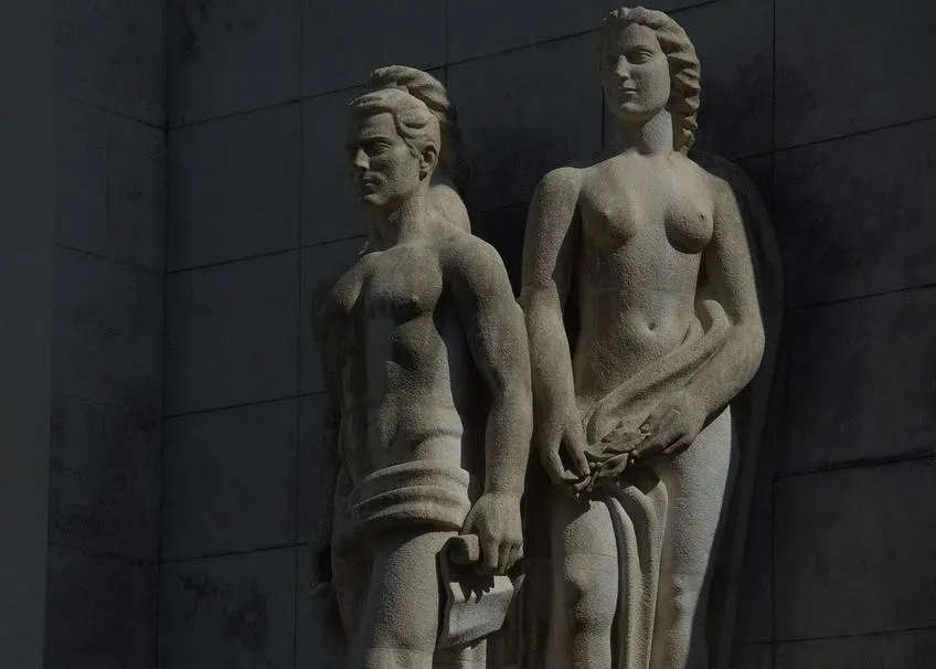 A close-up of a stone statue of a man and a woman, part of a larger monument, stands in the city.