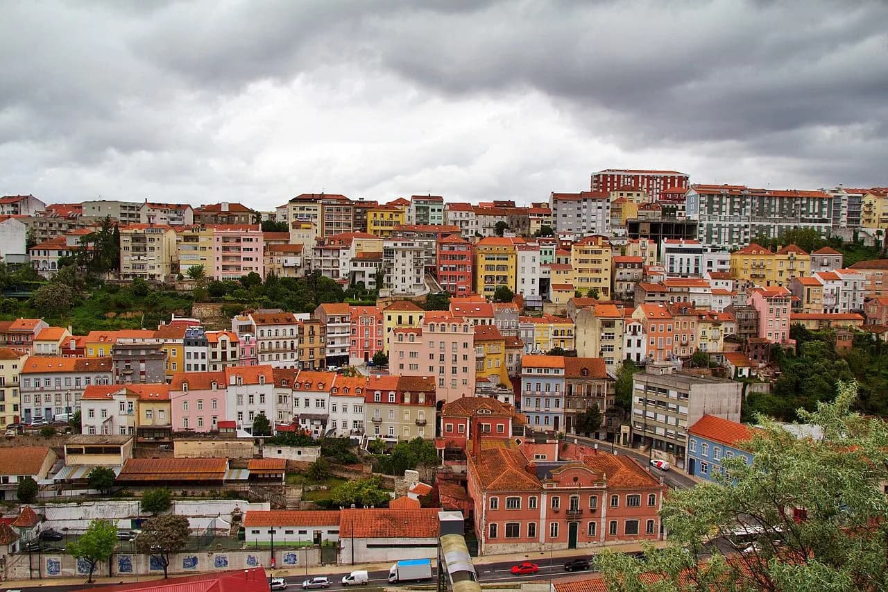 A panoramic view of Coimbra's hilly cityscape shows a dense cluster of traditional buildings with red-tiled roofs.