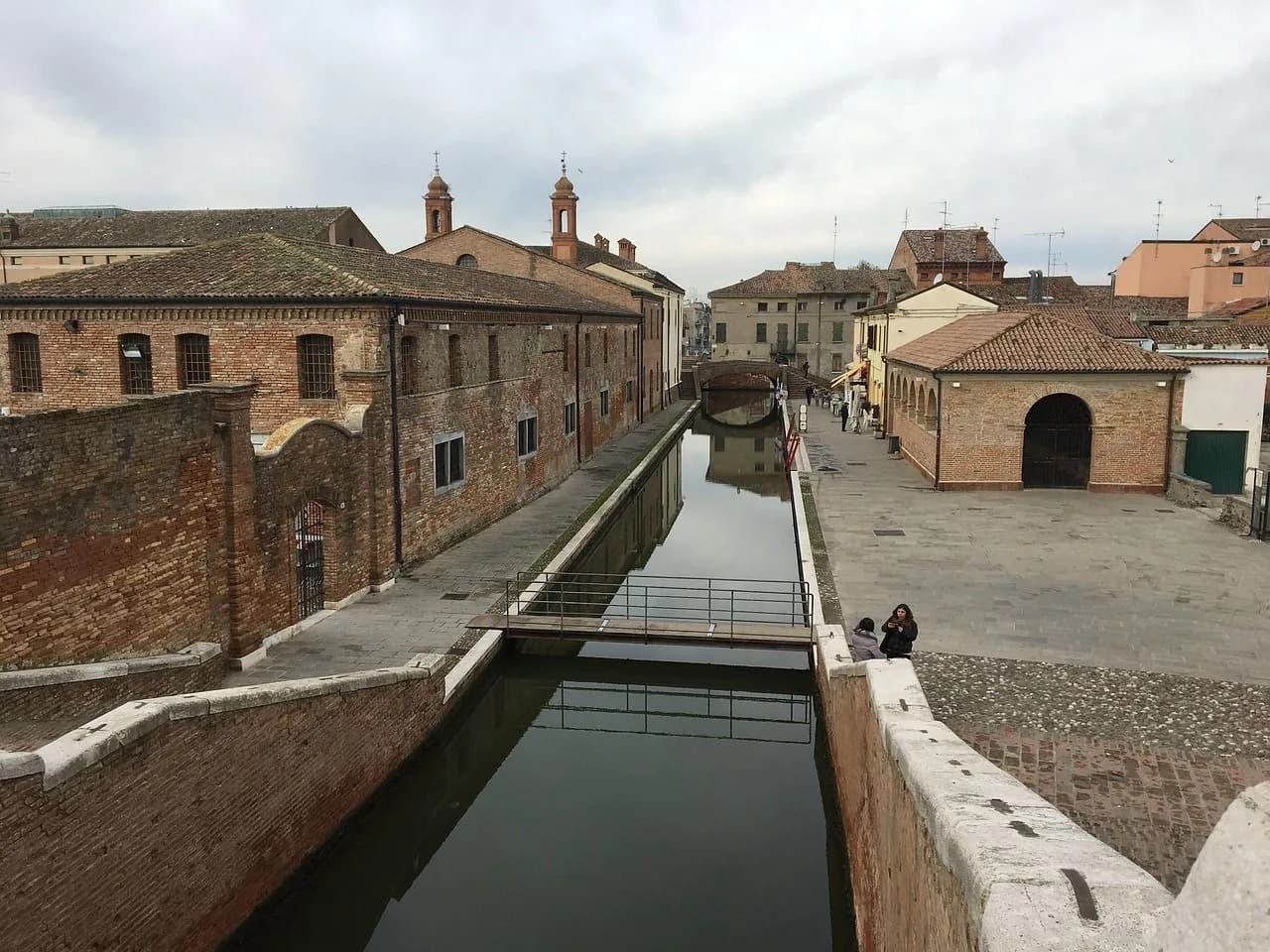 A tranquil canal in Comacchio is lined with historic brick buildings and a small footbridge.