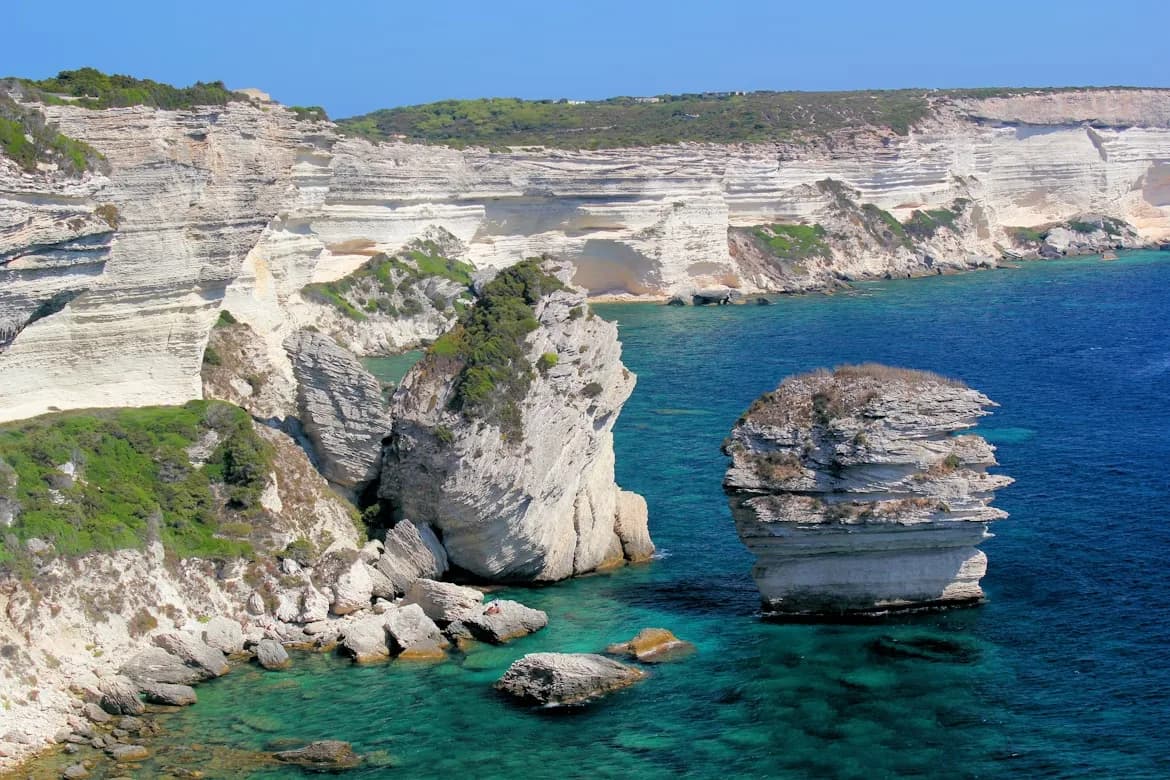 The stunning white cliffs of Bonifacio plunge into the turquoise waters, with impressive rock formations rising from the sea.