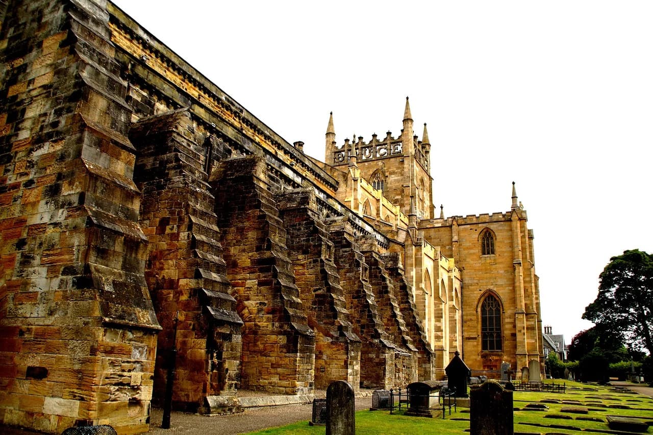 The stone facade and soaring buttresses of the historic Dunfermline Abbey are viewed from a low angle, highlighting its medieval architecture.