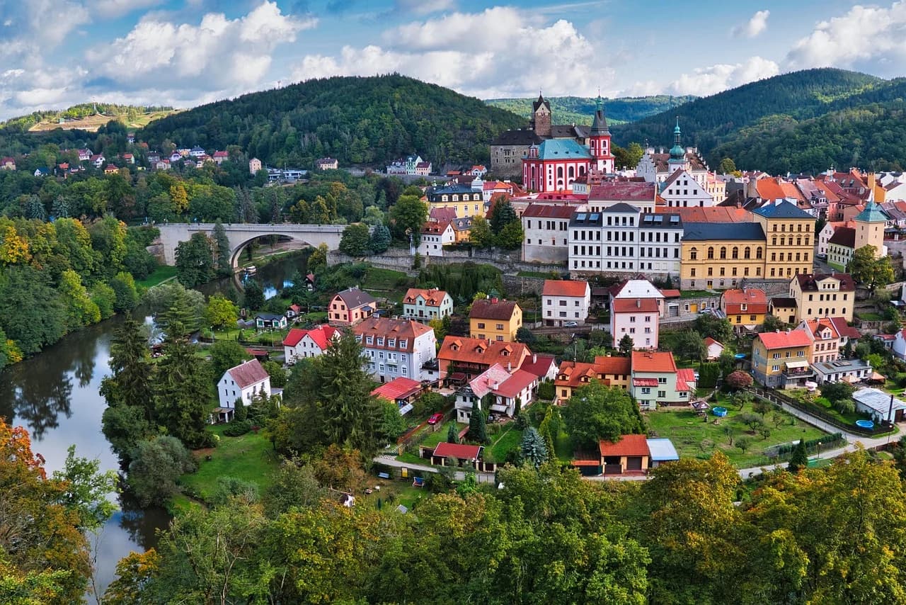 A picturesque view of a historic town nestled in a valley, with a river winding through it and a castle on a hill.
