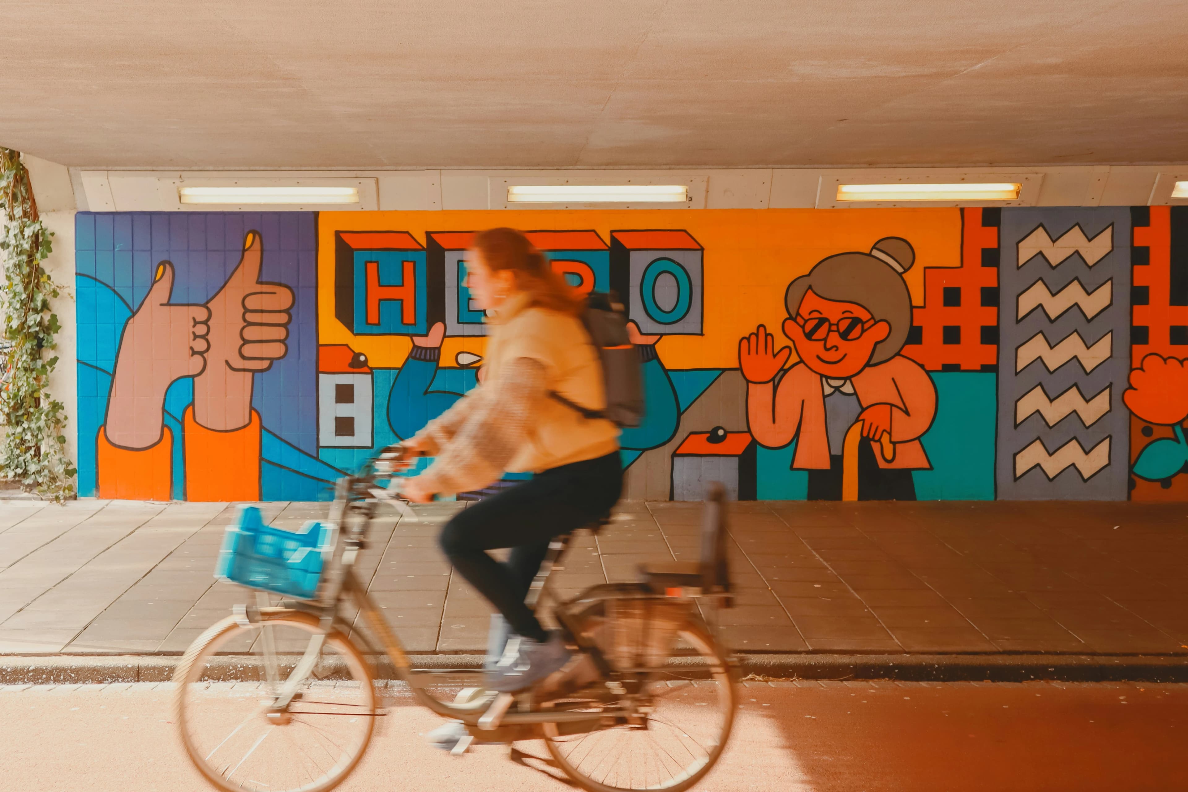 A person on a bicycle rides past a vibrant, multicolored mural in a modern underpass.