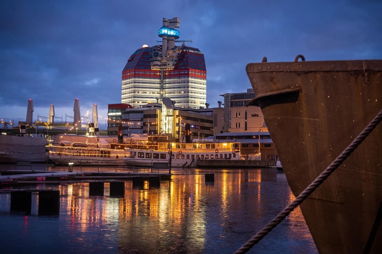 A modern skyscraper with red and white horizontal stripes is illuminated at night, reflected in the frozen harbor.