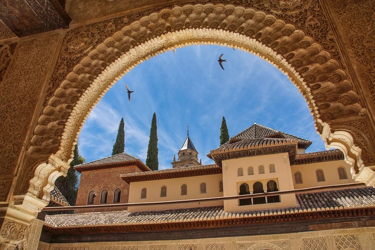 An intricate archway provides a framed view of the Patio de los Arrayanes in the Alhambra, with the serene pool reflecting the surrounding architecture.