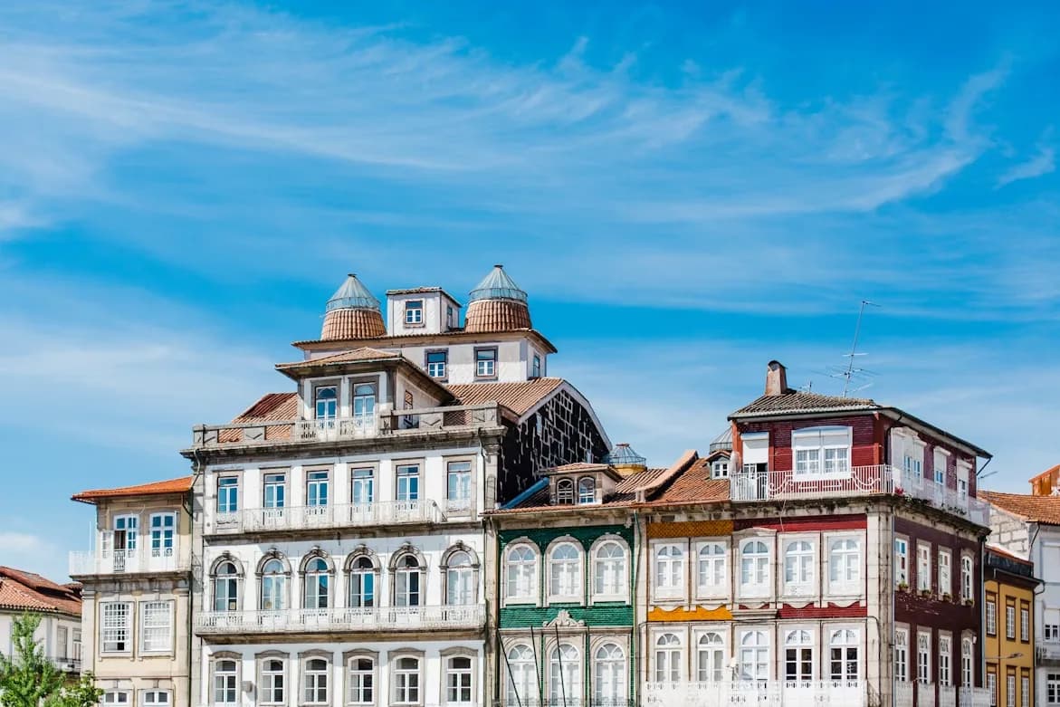 A row of colorful, traditional buildings with intricate iron balconies stands against a bright blue sky.